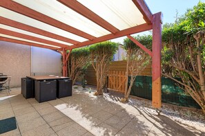 Une terrasse extérieure dotée d’un espace salon abrité, d’un barbecue et d’une clôture en bois.