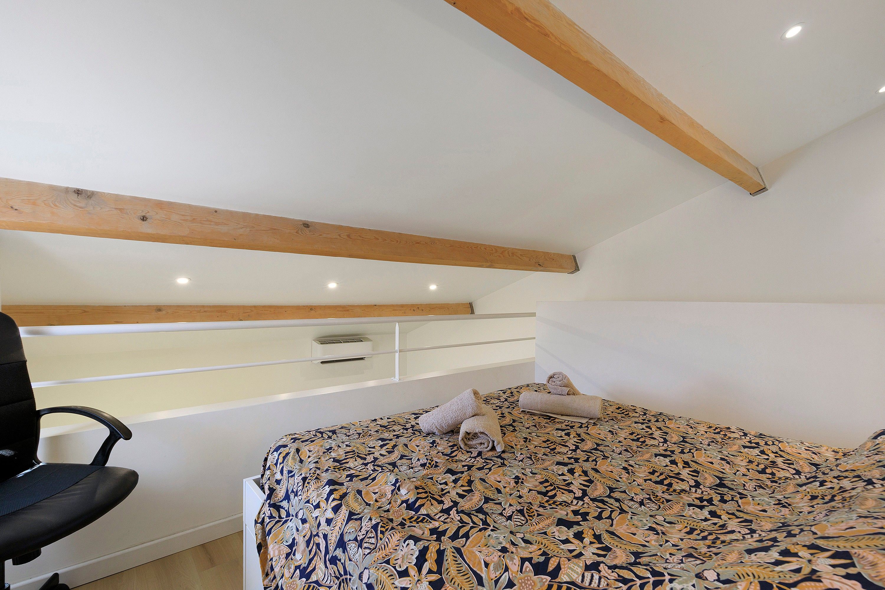 Un dormitorio con cama, una silla, un escritorio y un techo con vigas de madera.
