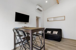 A compact living space with a flat-screen TV, a small dining table, foldable chairs, a sofa with decorative pillows, and a wooden floor. - Le patio du soleil: pool, tennis, A/C, private terrace, near beaches (Vic-la-Gardiole)