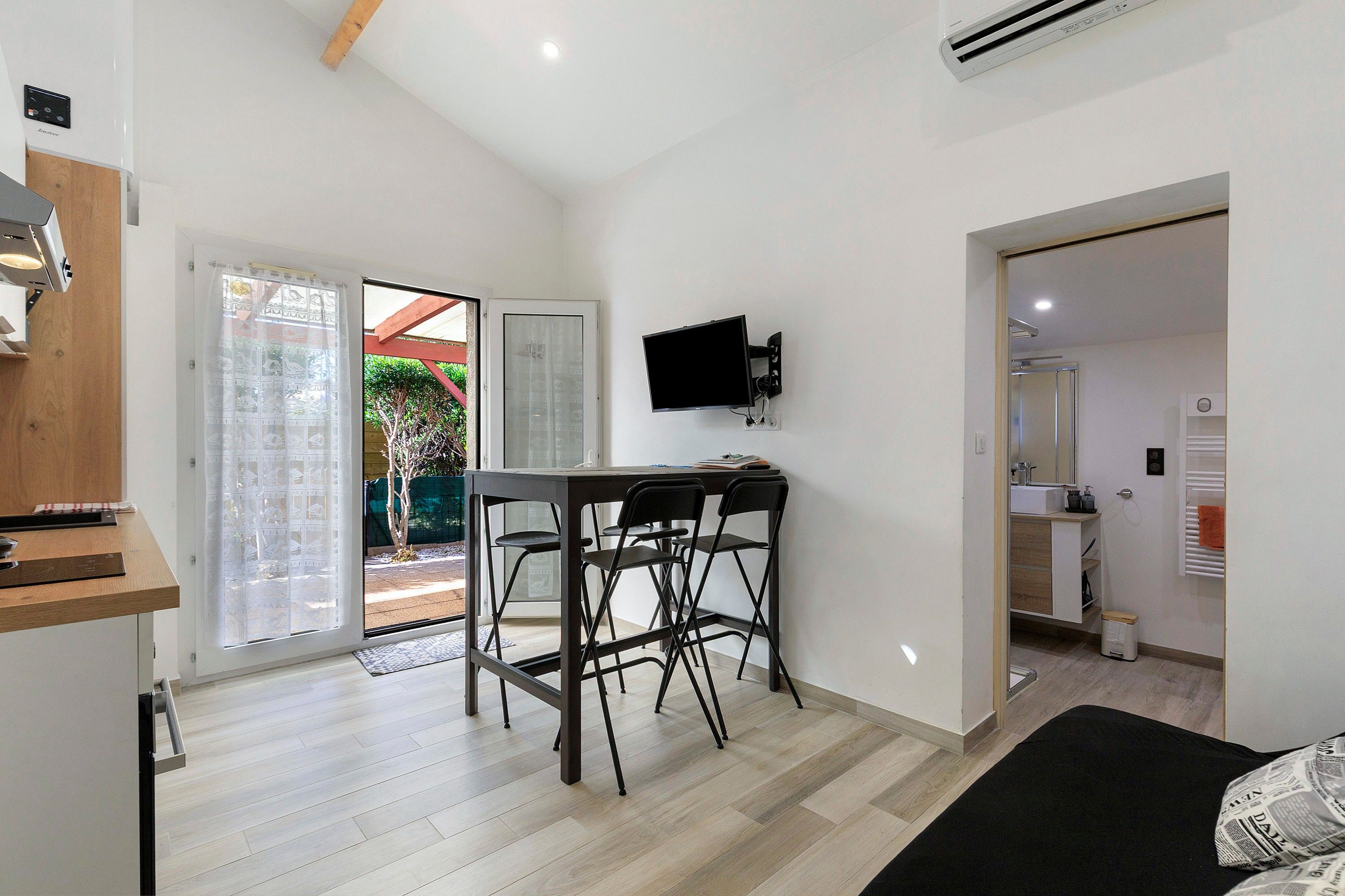 Un espacio habitable compacto con kitchenette, comedor con mesa y sillas, televisor de pantalla plana en la pared y puerta corrediza de vidrio que da a un área exterior.