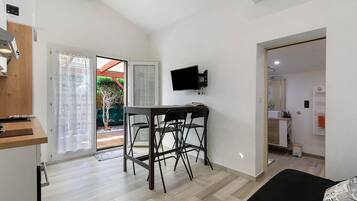 Un espacio habitable compacto con kitchenette, comedor con mesa y sillas, televisor de pantalla plana en la pared y puerta corrediza de vidrio que da a un área exterior.