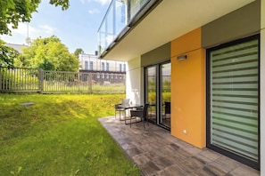 A modern outdoor patio with a table and chairs, a grassy area, and a building with large windows and a sliding door. - Cosy Apartment with Garden | Parking (Władysławowo)
