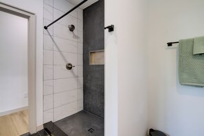 Casa de banho com chuveiro, paredes em azulejo, porta-toalhas e porta.