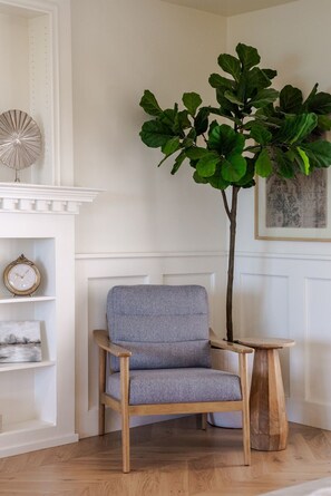 A room with a wooden chair, a small table, a large green plant, a clock, and a framed picture on the wall. - LUX Designer Oceanfront Estate in Long Beach - 4 Master Suites, Backyard Oasis (Long Beach)