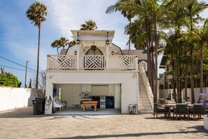 A two-story building with a covered outdoor seating area, a pool table, and a staircase leading to the upper level. - LUX Designer Oceanfront Estate in Long Beach - 4 Master Suites, Backyard Oasis (Long Beach)
