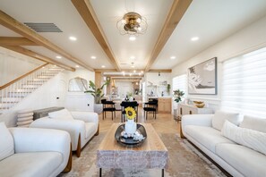 A spacious living room with a staircase, white sofas, a coffee table with decorative items, and a modern ceiling fan. - LUX Designer Oceanfront Estate in Long Beach - 4 Master Suites, Backyard Oasis (Long Beach)
