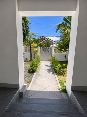 A pathway leading to a gated entrance with a house in the background, surrounded by greenery.