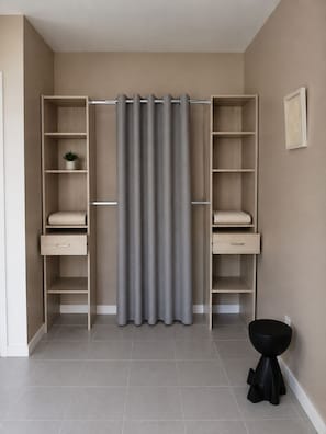 A walk-in closet with open shelving, a grey curtain, and a black stool. - Chez Mamette – Charming T2 Apartment with Terrace in the Heart of Provence. (Oraison)