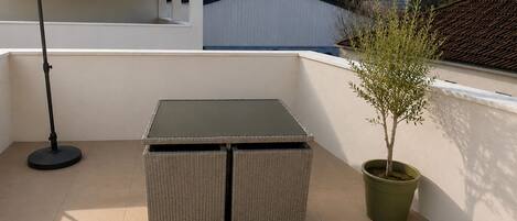 Een balkon met een tafel, stoelen, een plant in pot en een vloerlamp.