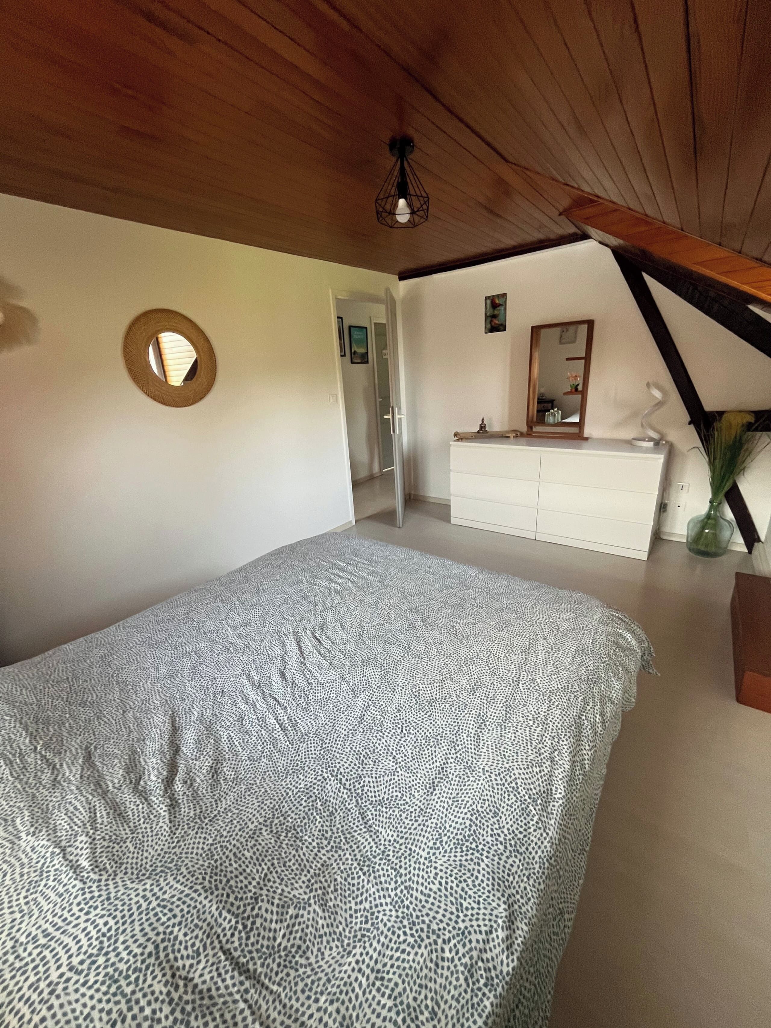 A bedroom with a bed, a dresser, a mirror, and a circular window.
