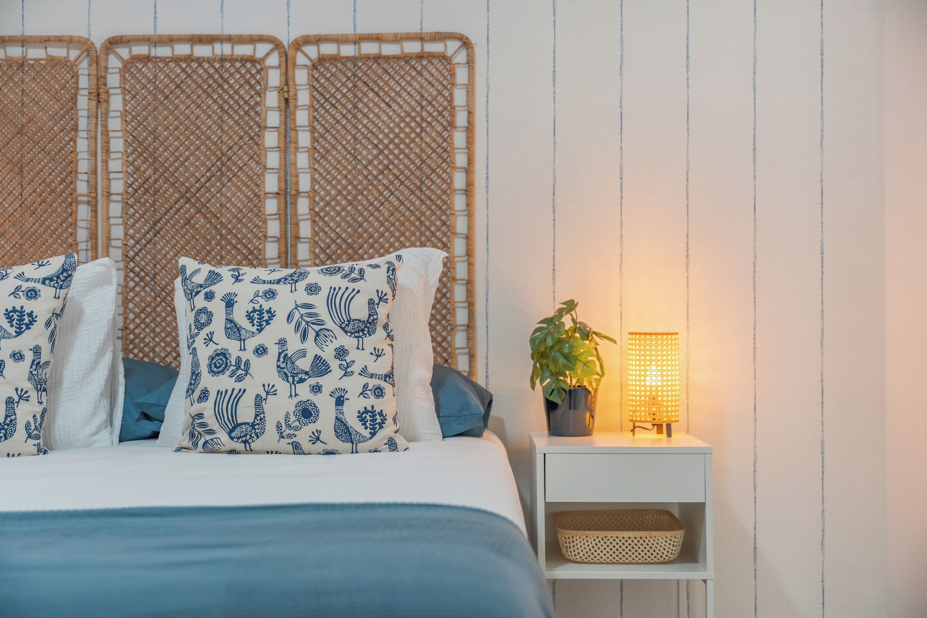 A bed with patterned pillows, a bedside table with a lamp, and a wicker headboard.