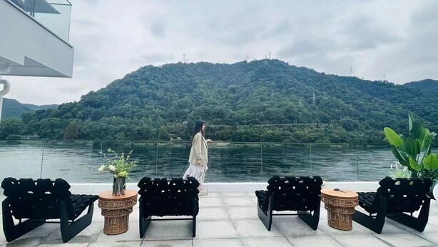 A terrace with outdoor seating, a view of a lake, and a forested hill in the background.