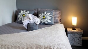 A neatly made bed with a large, textured blanket, two pillows with daisy designs, a small bedside table with a lamp, and a marble nightstand. - Double Room perfect for contractors and Professionals (West Midlands)