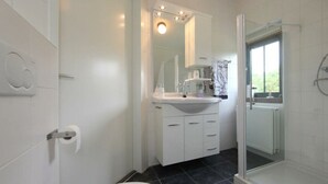 Ein Badezimmer mit Toilette, Waschbecken, Spiegel und Duschbereich.