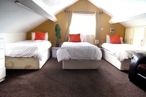 Ein Zimmer mit zwei Betten, einem großen Fenster, einer Pflanze und einem Deckenventilator.