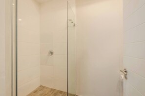 Une cabine de douche fermée par des parois en verre, avec des murs recouverts de carreaux blancs et une pomme de douche visible.