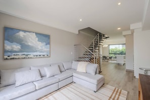 Un salon moderne avec un canapé d’angle, un escalier et un coin repas.