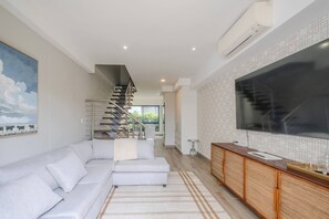 Un salon moderne avec un canapé, un escalier, un téléviseur et un coin cuisine.