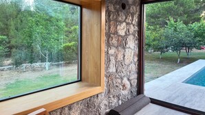 Ein Zimmer mit Steinwand, einer Holzbank, einem großen Fenster und Blick auf einen Swimmingpool.
