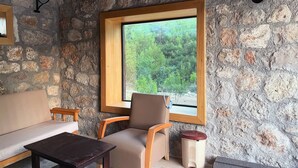 Ein Zimmer mit Steinwänden, einem Holzkrahmenfenster, einer Couch, einem Sessel und einem kleinen Tisch.