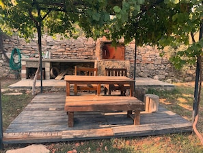 A rustic outdoor seating area with a stone wall, wooden table and benches, and a pergola with grapevines. - Escape the noise, hear only nature’s voice (Karacahisar)