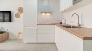 A modern kitchen with white cabinetry, a wooden countertop, a built-in microwave, and a wall-mounted television. - Cozy Apartment Rental in Guargacho, Spain - Ideal Family Stay (Guargacho)