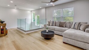 Uma sala de estar moderna com um sofá seccional, uma mesa de centro redonda e um guarda-corpo de vidro.