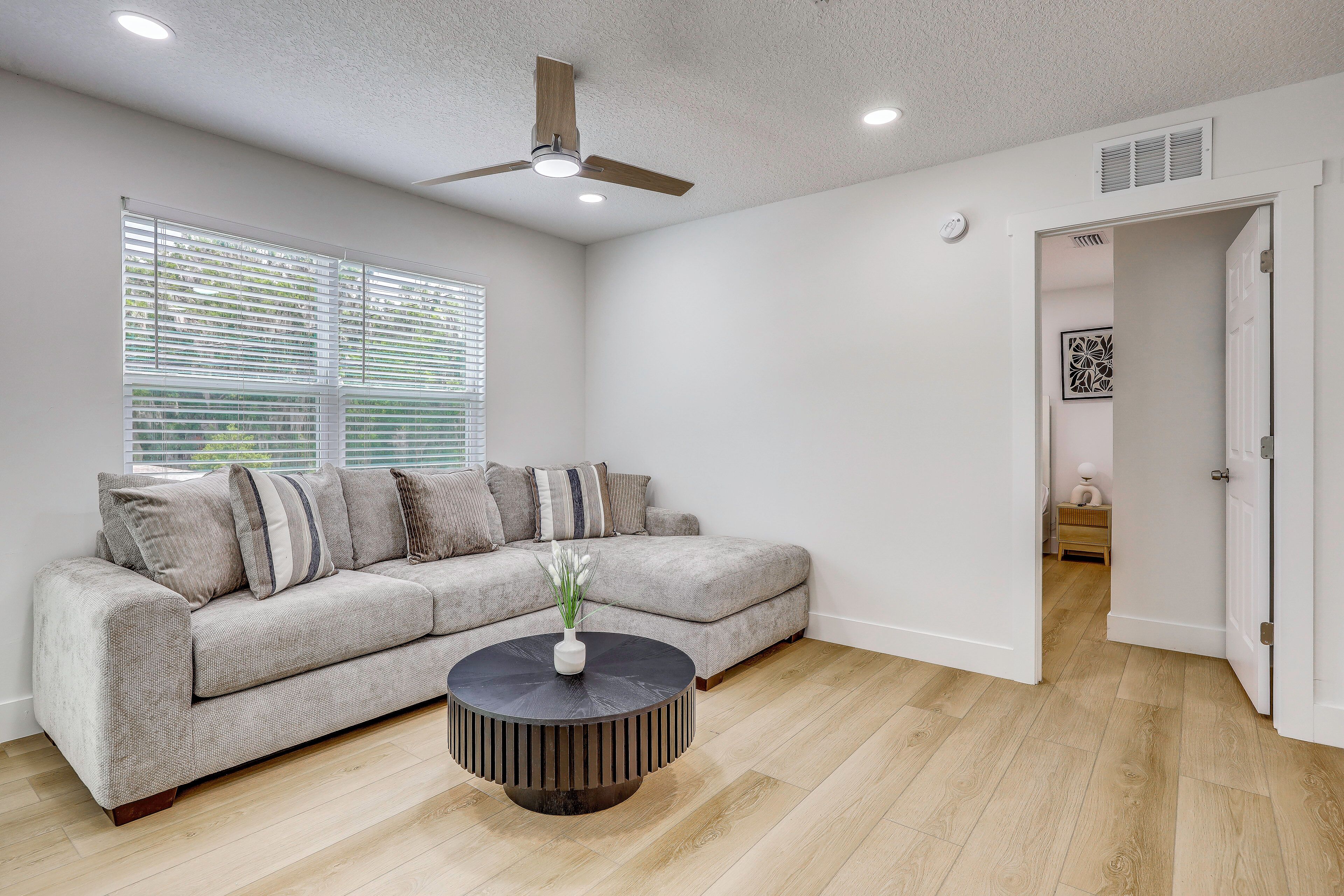 Un salon moderne avec un canapé d’angle, une table basse ronde et un ventilateur de plafond.