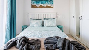 Un dormitorio con cama, mesita de noche, armario y un cuadro de olas.