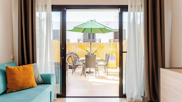Habitación con puerta de vidrio corredera que da a un espacio exterior con mesa, sillas y sombrilla.