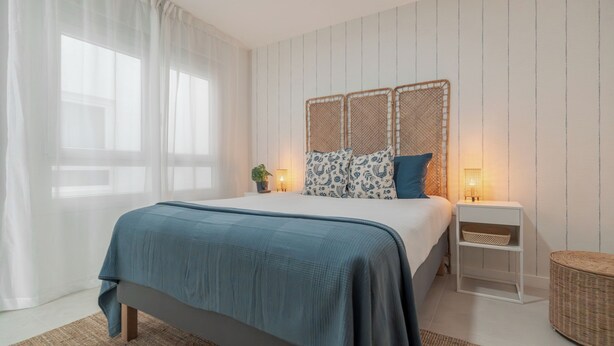 Quarto com cama, mesas de cabeceira, luminária e janela com cortinas.