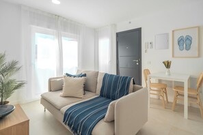 Ein modernes Wohnzimmer mit einer Couch, einem Esstisch mit Stühlen, einer Tür und einem gerahmten Bild an der Wand.