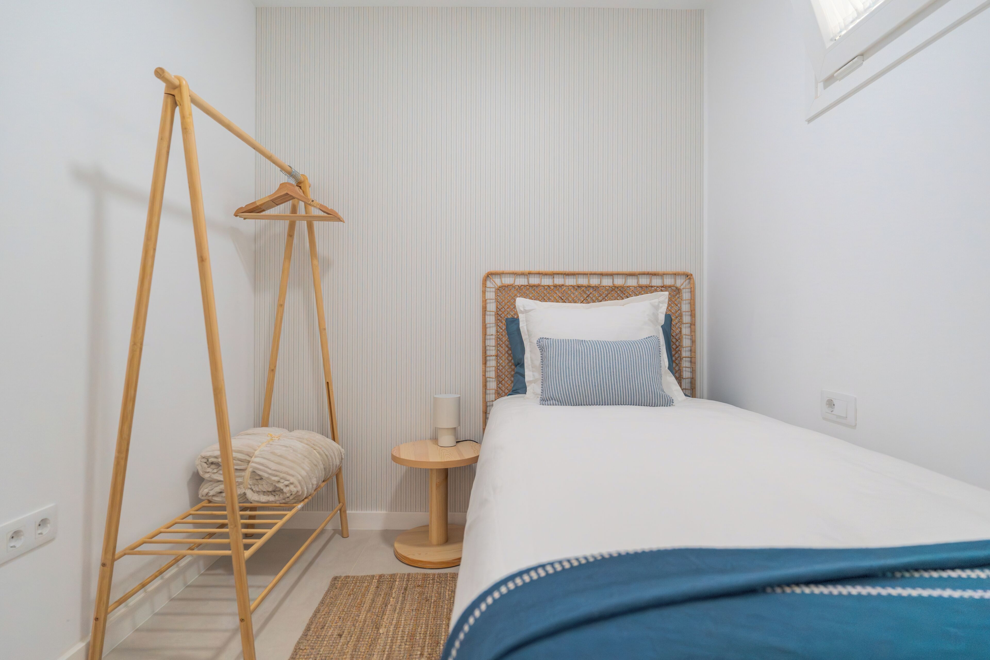 A bedroom with a bed, a hanging clothes rack, a bedside table, and a window.