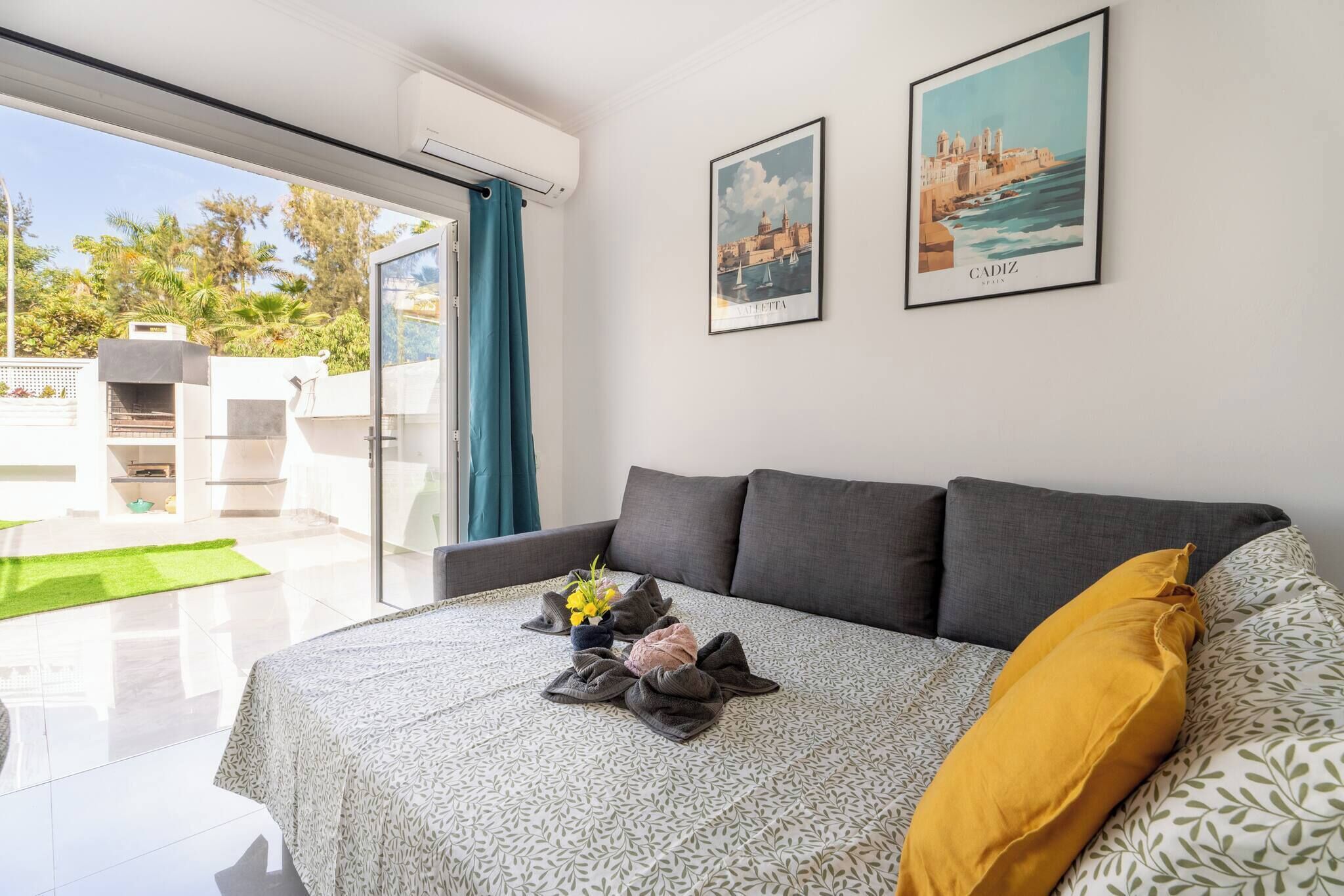 Ein modernes Zimmer mit einer Couch, einem Bett mit gemustertem Überwurf, einem Stadtbild in einem Rahmen und einem Grill draußen.
