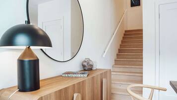 A modern interior with a wooden console table, a black lamp, a mirror, a vase, and a staircase.