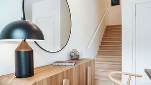 Ein modernes Interieur mit einem Holztischchen, einer schwarzen Lampe, einem Spiegel, einer Vase und einer Treppe.