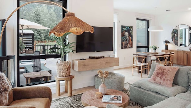 Ein modernes Wohnzimmer mit Fernseher, Sofa, Esstisch und großen Fenstern.