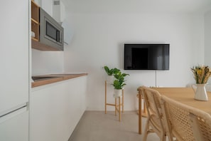 A modern kitchen with white cabinetry, a wooden countertop, a built-in microwave, a wall-mounted TV, and a dining area with a wooden table and wicker chairs. - 2-Bedroom Apartment in Guargacho, Tenerife sur (Guargacho)