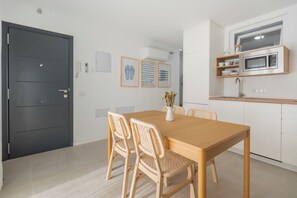 A modern kitchen with a microwave, a sink, and a dining area with a wooden table and wicker chairs. - 2-Bedroom Apartment in Guargacho, Tenerife sur (Guargacho)