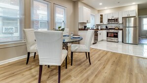 A modern kitchen with white cabinets, stainless steel appliances, and a dining area with a glass table and white chairs. - Family-Friendly Detroit Duplex: Walk to Parks! (Detroit)