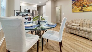 A dining area with a glass table, white chairs, and a kitchen in the background. - Family-Friendly Detroit Duplex: Walk to Parks! (Detroit)