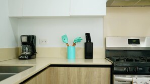 A kitchen with a coffee maker, a teal utensil holder, and a stove. - El mar te llama · 2BR Los Corales (Punta Cana City)