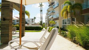 A resort with outdoor lounge chairs, a pool, and a building with balconies. - El mar te llama · 2BR Los Corales (Punta Cana City)