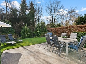 Eine Terrasse mit Tisch und Stühlen, umgeben von einem gepflegten Rasen und Hecken.