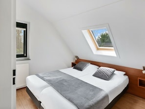 Ein Schlafzimmer mit schrägen Wänden, einem Oberlicht und einem Bett mit zwei Kissen sowie einem Nachttisch.