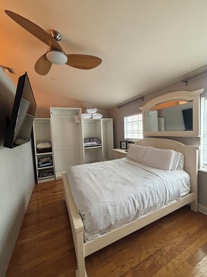 A bedroom with a bed, a wardrobe, a mirror, a ceiling fan, and a television.