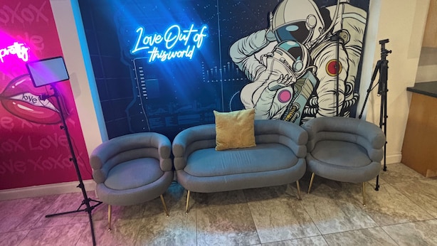 A room with a blue wall featuring a neon sign and a mural of an astronaut. There is a grey sofa with a pillow and a microphone stand. - THE ONLY HOUSE IN CHANNELSIDE BY WATER STREET (Tampa)