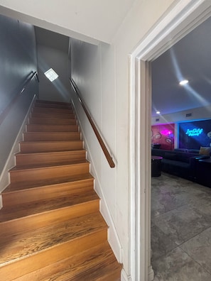 A wooden staircase with a handrail leading to a room with a neon sign.