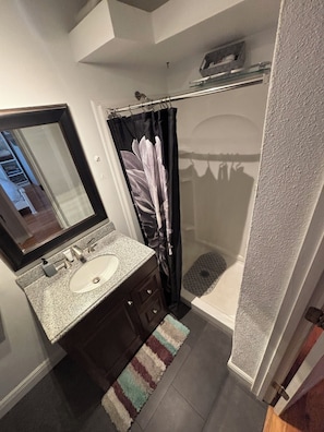Ein Badezimmer mit Marmorwaschtisch, einem Spiegel, einer Dusche mit Glastür und einem Streifenmuster-Teppich auf dem Boden.