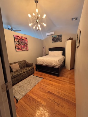 Ein Schlafzimmer mit Bett, Sofa, Teppich, einer Deckenleuchte und Kunstwerken an den Wänden.